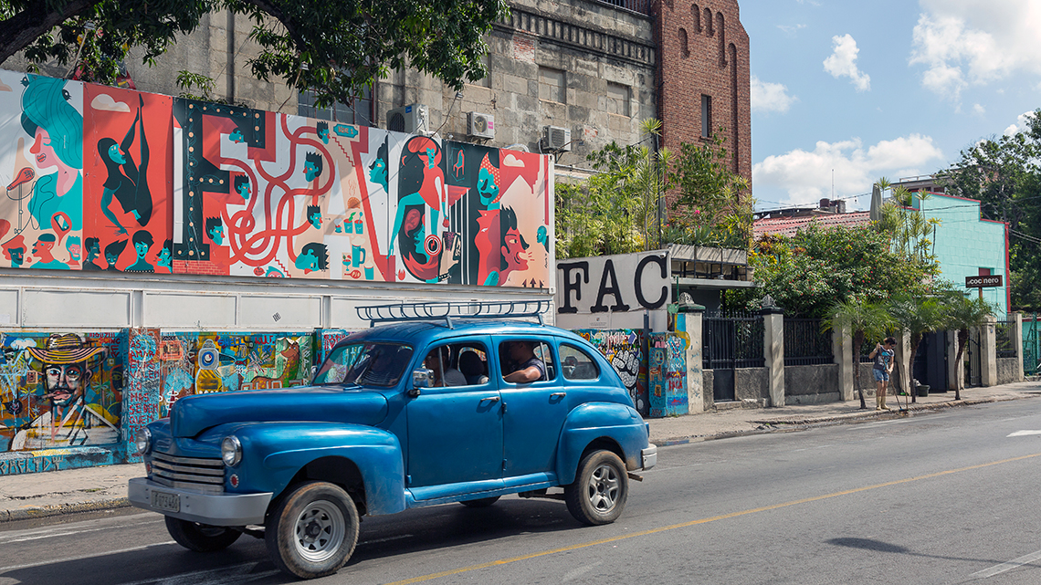 Vintage american car from 40s cruising the streets of Havana, in the background Fabrica de Arte Cubano